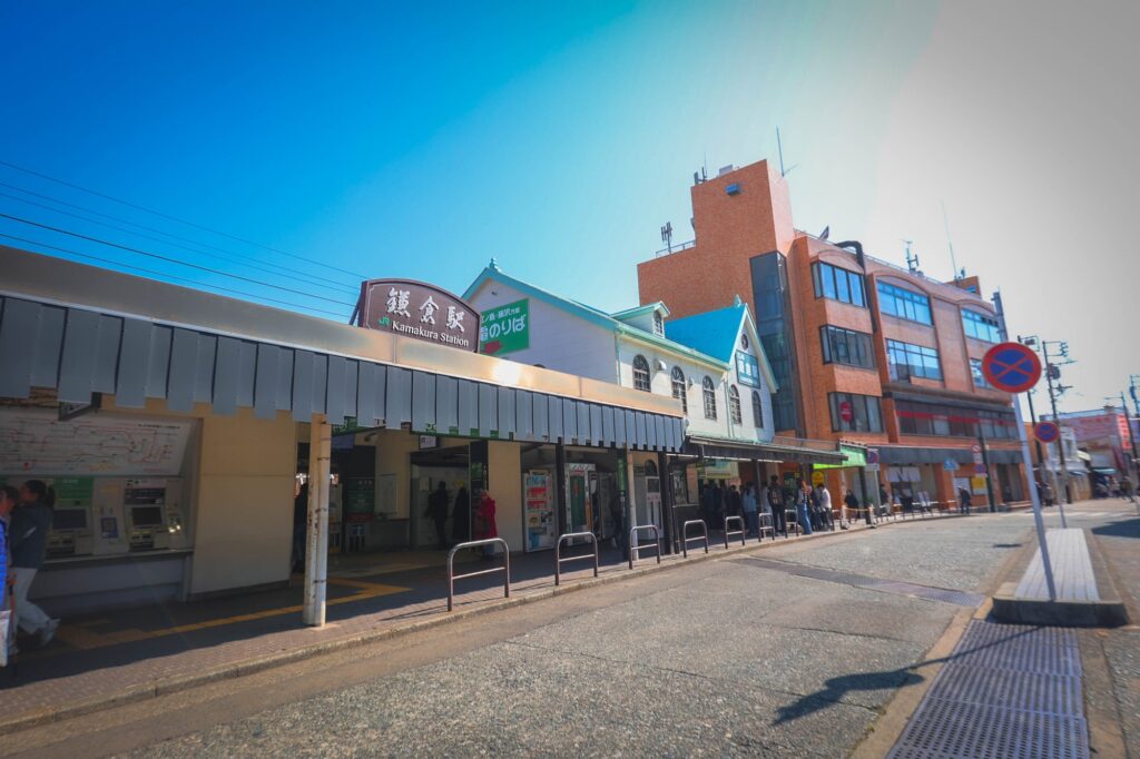 青空の下、レトロな時計台と緑の屋根が特徴的なJR鎌倉駅の駅舎外観と駅前の様子。