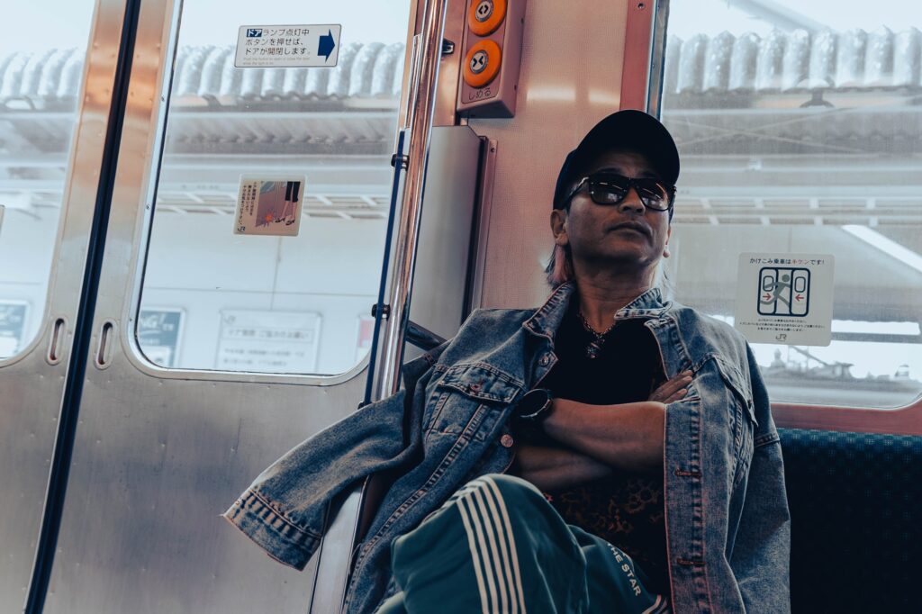 相模湖の静寂、西八王子の熱。仲間と囲む「痛風鍋」で締める、最高の休日。 中央線の車内、腕組みをして座るデニムジャケットにサングラス姿の男性。