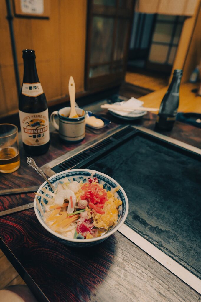 八王子のお好み焼き店。テーブルの鉄板を前に、海老や紅生姜が鮮やかに盛られたボウルと、瓶ビール、グラスが置かれた、食欲をそそる夕食の風景。