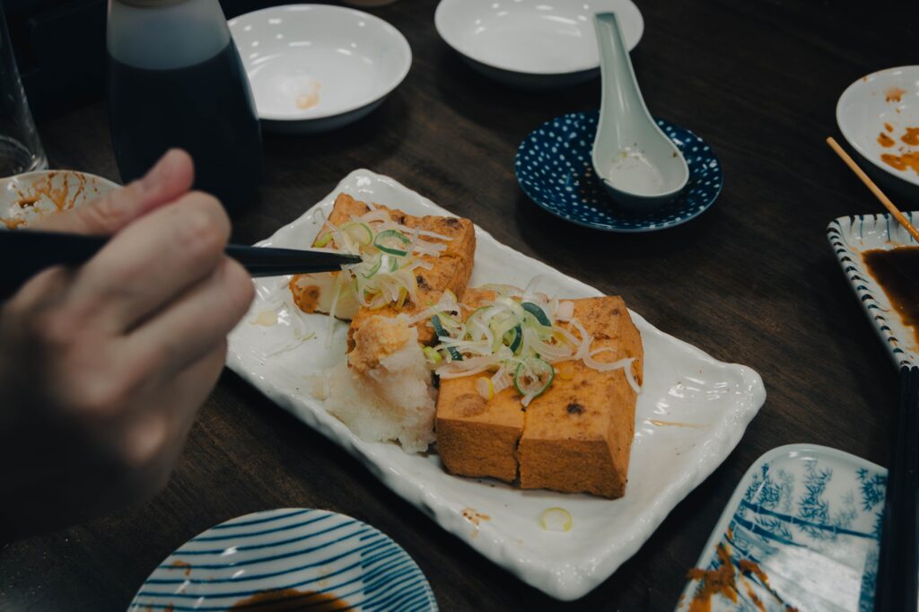 八王子、酒蔵「一平」。昭和の重低音とカメラ談義。 白い皿に盛られた、たっぷりのネギとおろしが添えられた厚揚げ。箸で今まさに食べようとしている瞬間の接写。