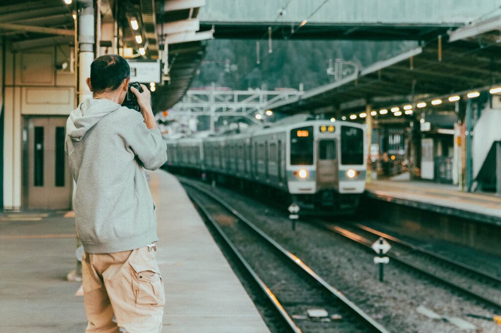 相模湖の静寂、西八王子の熱。仲間と囲む「痛風鍋」で締める、最高の休日。 夕暮れが迫る相模湖駅のホーム。通過する列車に狙いを定め、低い姿勢でシャッターを切るカメラマンの背中。