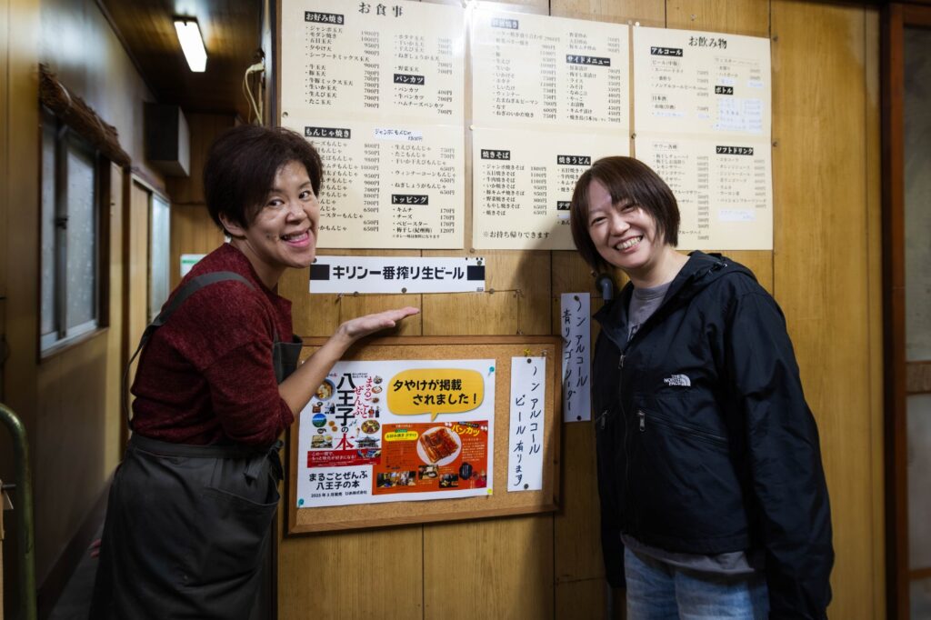 黄色い看板が灯る夜。八王子「夕やけ」で見つけた、昭和の温もり。 hachioji yuyake two women pointing at wall menu board