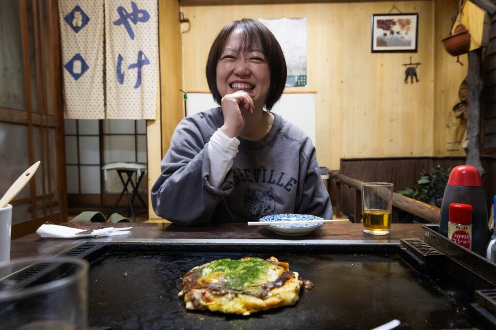 黄色い看板が灯る夜。八王子「夕やけ」で見つけた、昭和の温もり。 hachioji yuyake interior with woman enjoying okonomiyaki